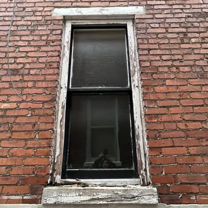 Old window in a brick wall with badly rotted, peeling wood trim before replacement in York, Pennsylvania